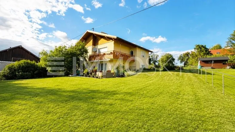 Gelbes Einfamilienhaus mit großem grünen Garten und Balkon unter blauem Himmel.