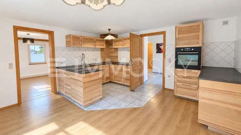 Offene Küche mit Holzschränken, integriertem Backofen und Übergang zu weiteren Räumen.