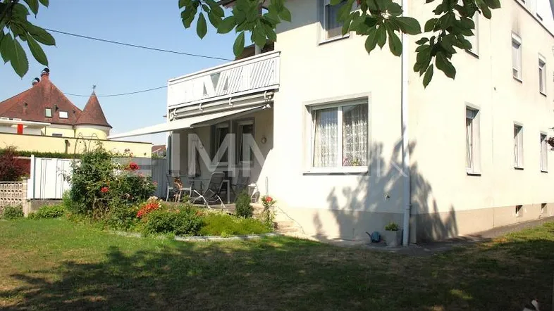 Außenansicht eines Hauses mit gepflegtem Garten, kleiner Terrasse und Balkon im Obergeschoss.