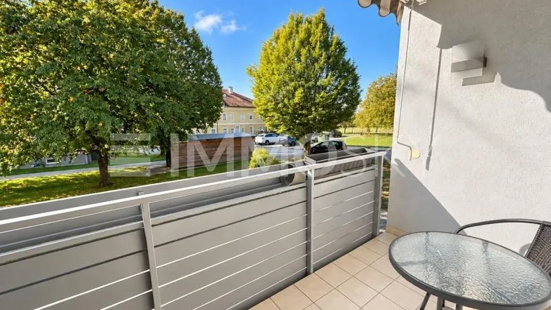 Heller Balkon mit Fliesenboden, Markise und Blick ins Grüne, ausgestattet mit einem kleinen Tisch.