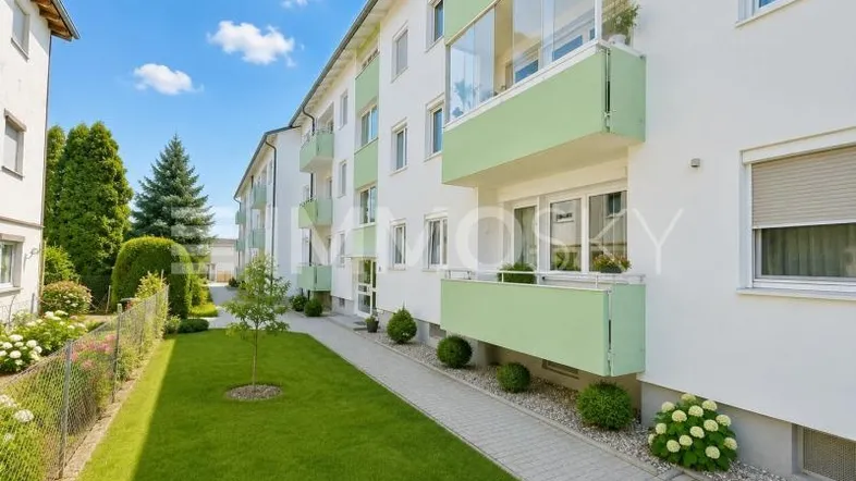 Mehrfamilienhaus mit gepflegter Grünfläche und Balkonen in hellgrün unter blauem Himmel.