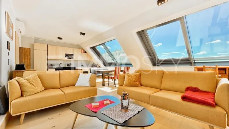 Helles, offenes Wohnzimmer mit integrierter Küche, Holzboden und großen Dachfenstern.