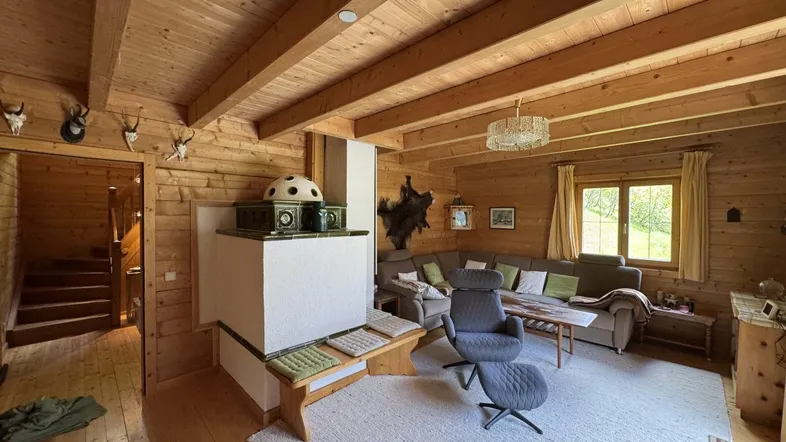 Geräumiges Wohnzimmer mit Kachelofen, Holzwänden und Treppenzugang in traditionellem Stil.