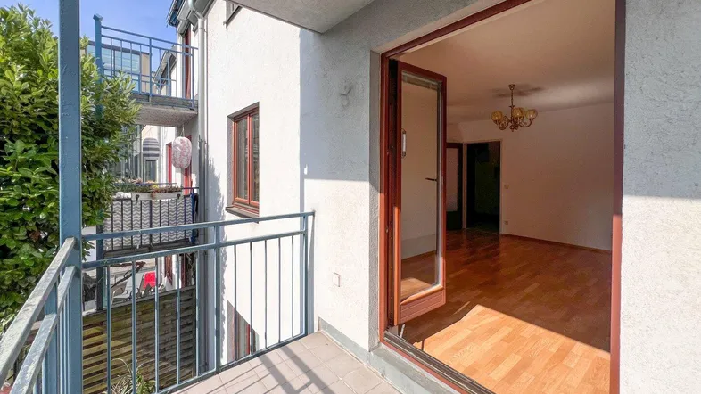 Heller Wohnbereich mit Parkettboden und Zugang zu einem sonnigen Balkon, ideal für entspannte Stunden.