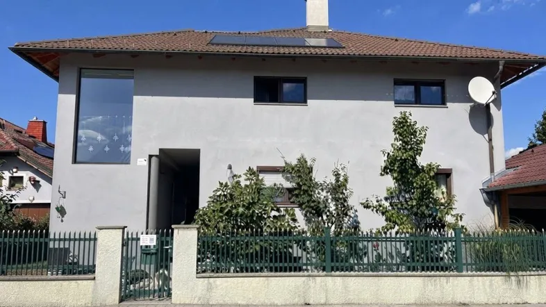 Modernes Einfamilienhaus mit grauer Fassade, großen Fenstern und einem gepflegten Vorgarten.