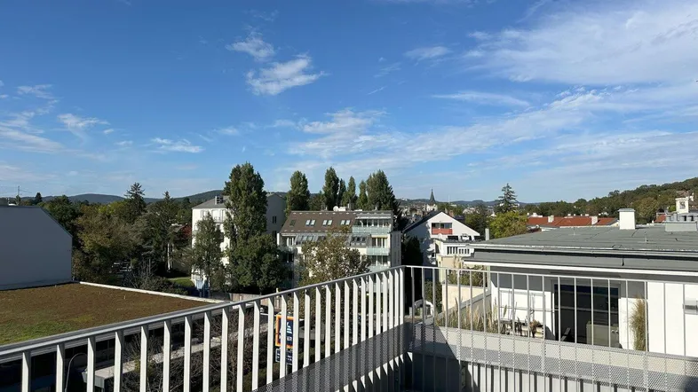 Geräumige Dachterrasse mit Metallgeländer und weitem Blick über die Stadt und grüne Hügel.