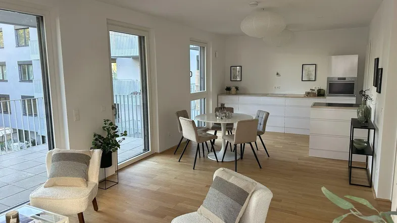 Offener Wohn-Essbereich mit Küche, Holzboden und Zugang zu einem Balkon.