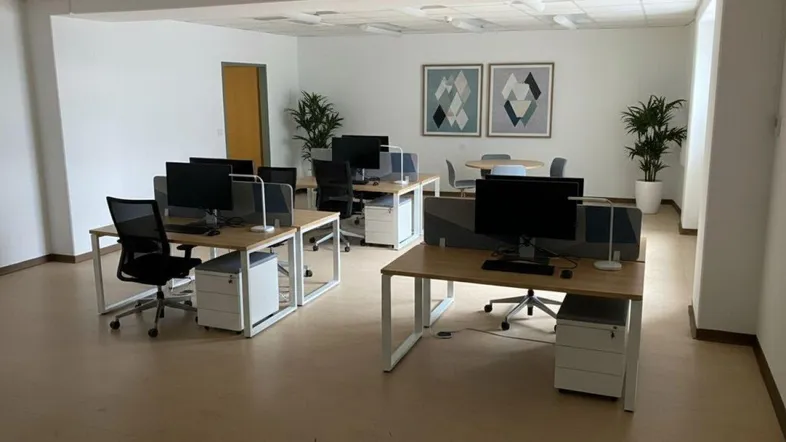 Großes, offenes Büro mit mehreren Arbeitsplätzen, modernen Schreibtischen und einem kleinen Besprechungsbereich.