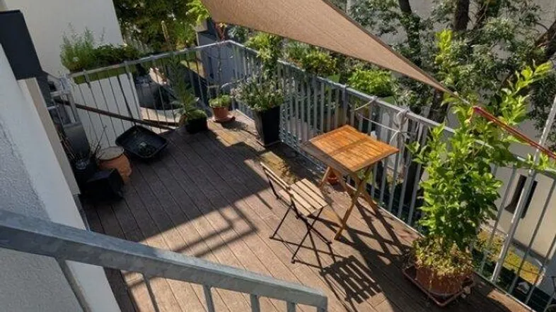 Helle Dachterrasse mit Holzbelag, Sonnensegel und Blick auf die umliegenden Gebäude und Bäume.
