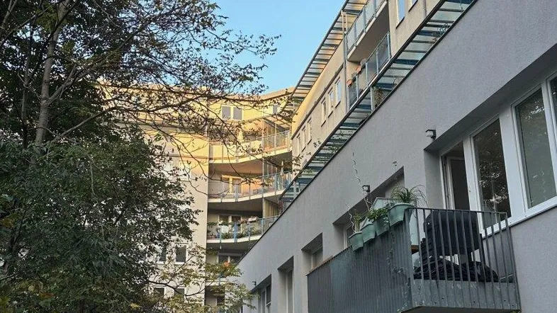 Moderne Wohnanlage mit Balkonen und begrüntem Innenhof, umgeben von Bäumen unter blauem Himmel.