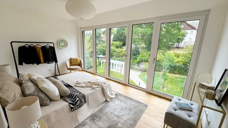 Helles Schlafzimmer mit großen Fenstern, die einen direkten Blick in den grünen Garten bieten.