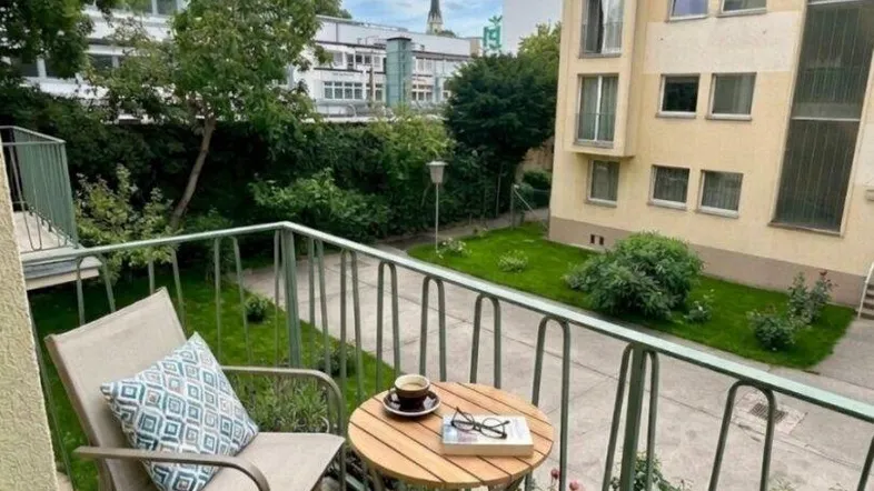 Gemütlicher Balkon mit Sitzgelegenheiten und Blick auf die umliegenden Gebäude und Grünflächen.
