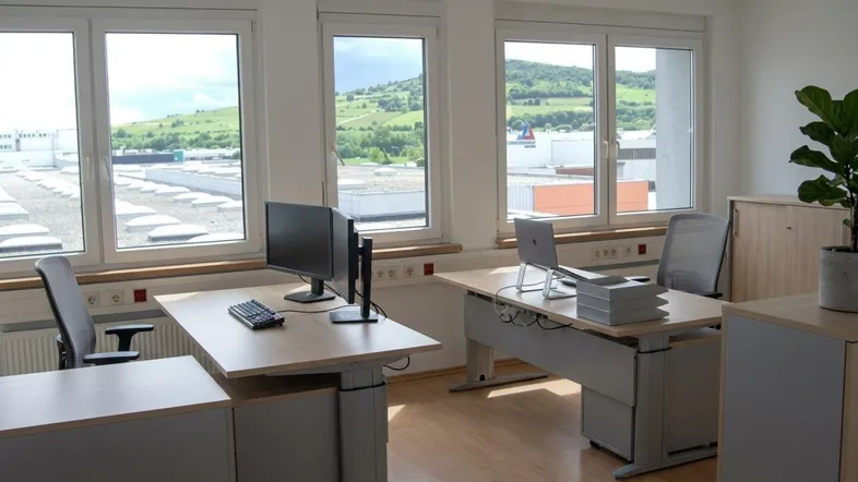 Modernes Büro mit mehreren Arbeitsplätzen, großen Fenstern und Blick auf die grüne Umgebung.