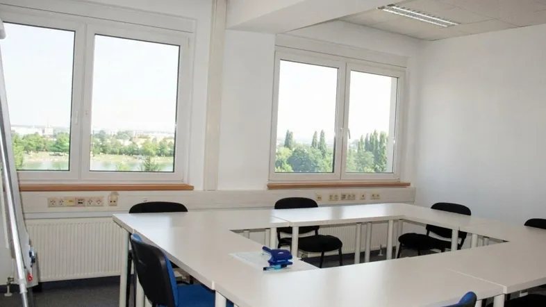 Heller Büroraum mit U-förmigem Konferenztisch, großen Fenstern und Blick auf Wasser und Grünflächen.