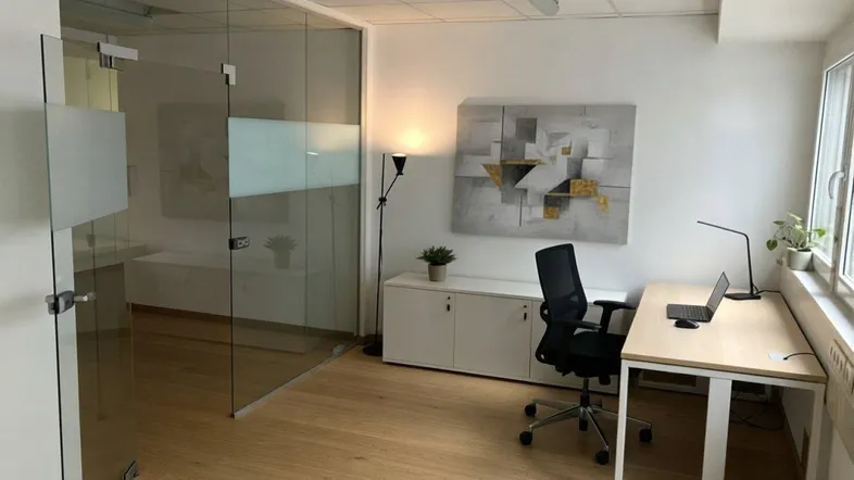 Modernes Büro mit Glaswänden, Holzboden und einem Arbeitsplatz mit Laptop.