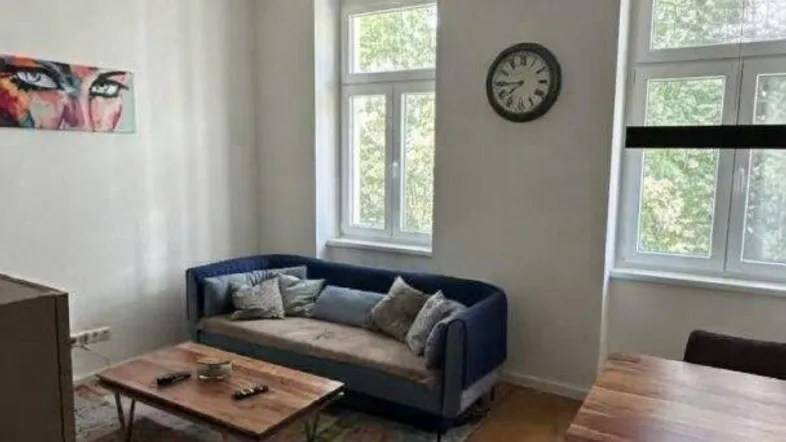 Helles Wohn- und Esszimmer mit Holzboden, bequemer Couch und Esstisch am Fenster.