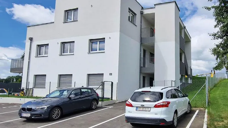 Modernes Mehrfamilienhaus mit weißer Fassade und Parkplätzen im Freien.