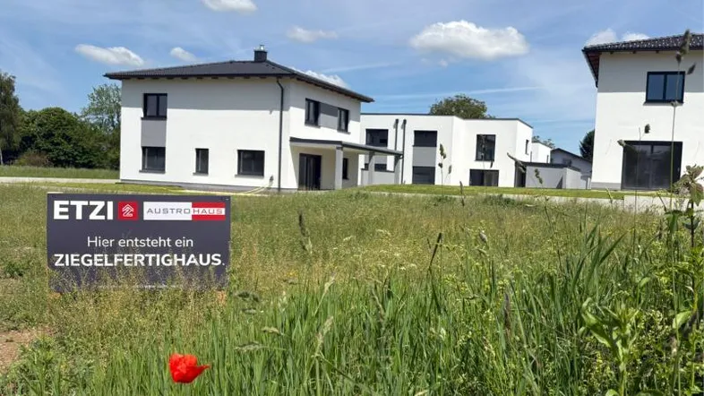 Neubau eines Ziegelfertighauses auf einem Grundstück mit weiteren Häusern im Hintergrund.