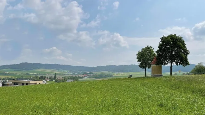 Weitläufige grüne Landschaft mit Hügeln und einem kleinen Gebäude unter blauem Himmel.