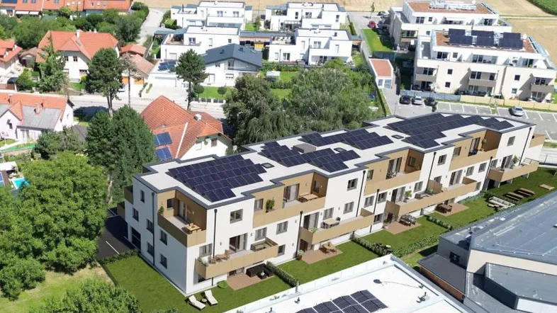 Luftaufnahme eines modernen Wohnkomplexes mit Photovoltaikanlagen auf den Dächern und umliegender Landschaft.