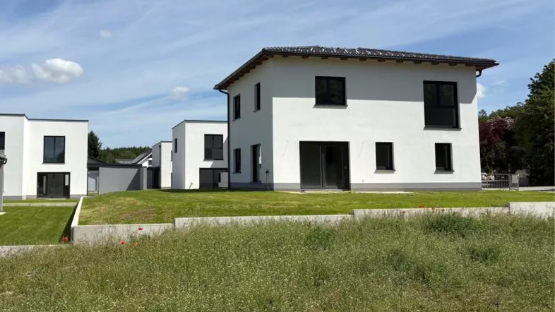 Modernes weißes Einfamilienhaus mit dunklem Dach und gepflegtem Rasen unter blauem Himmel.
