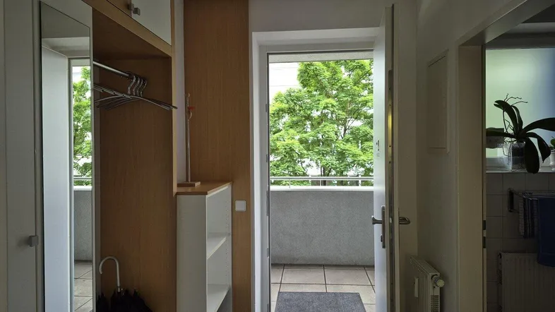 Eingangsbereich mit Garderobe und direktem Zugang zu einem sonnigen Balkon mit grüner Aussicht.