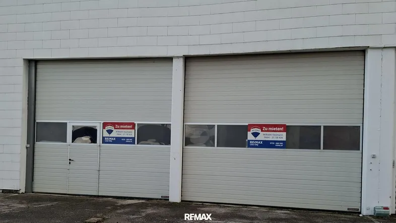 Zwei große Garagentore mit "Zu vermieten"-Schildern an einer weißen Gewerbeimmobilie.