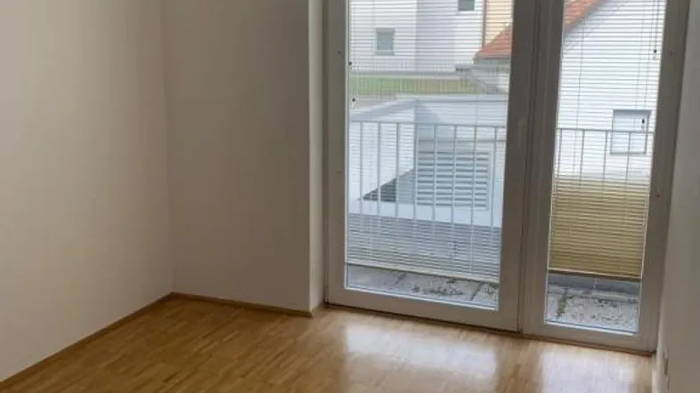 Helles Zimmer mit Parkettboden und Zugang zu einem kleinen Balkon, ideal als Schlaf- oder Wohnbereich.