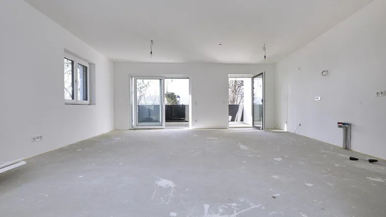 Heller, unfertiger Wohnbereich mit großen Schiebetüren und Zugang zu einem Balkon.