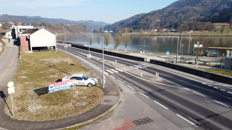 Luftaufnahme einer Straße entlang eines Flusses mit Bergen im Hintergrund und einem Maklerbanner.