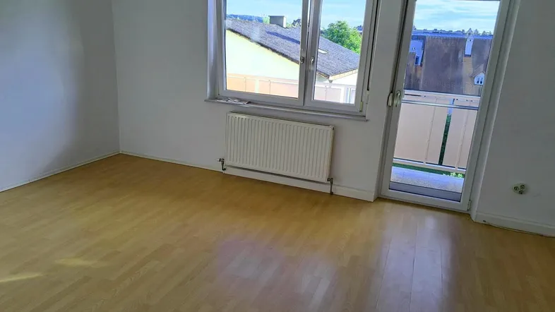 Helles Zimmer mit Laminatboden, Heizkörper und Zugang zu einem Balkon.