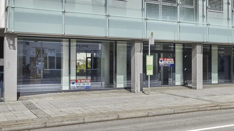 Moderne Geschäftsfassade mit großen Schaufenstern und "ZU MIETEN"-Schildern, direkt an einer belebten Straße gelegen.