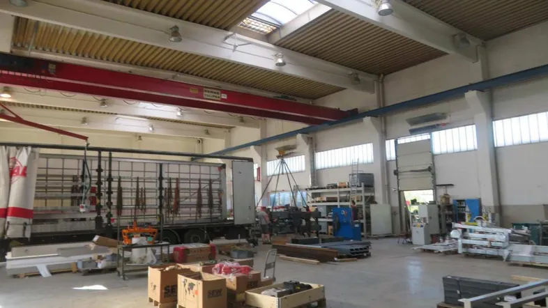 Geräumige Lagerhalle mit hohen Decken, Oberlichtern und einem Kran, gefüllt mit Materialien und einem LKW.