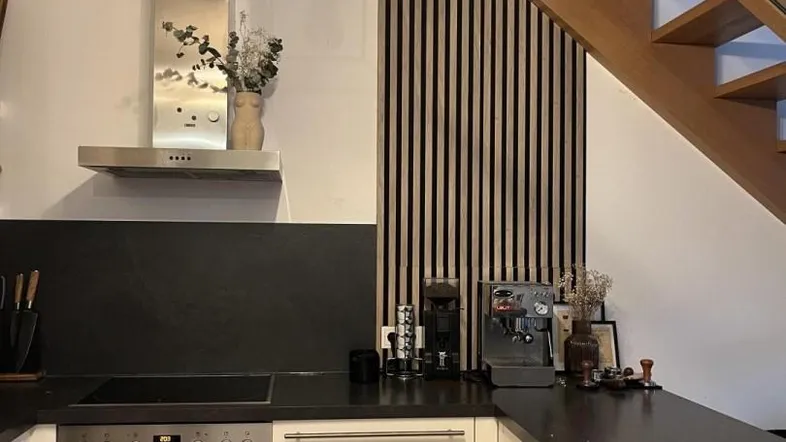 Moderne Küche mit dunkler Arbeitsplatte, integriertem Backofen und einer Holzlamellenwand neben der Treppe.