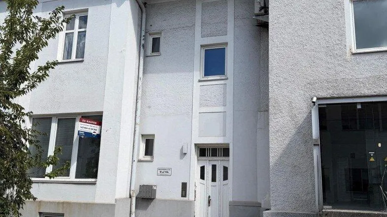 Fassade eines Mehrfamilienhauses mit Eingangsbereich und Fenstern, teilweise mit Vermietungsschild.