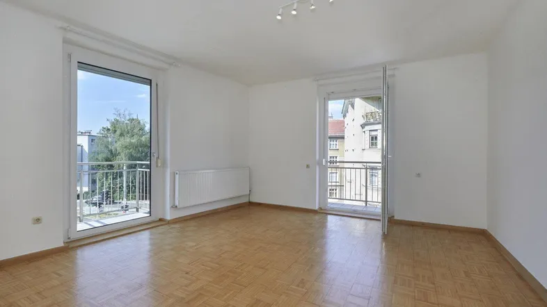 Helles Zimmer mit Parkettboden und Zugang zu zwei französischen Balkonen, ideal als Wohn- oder Schlafzimmer.