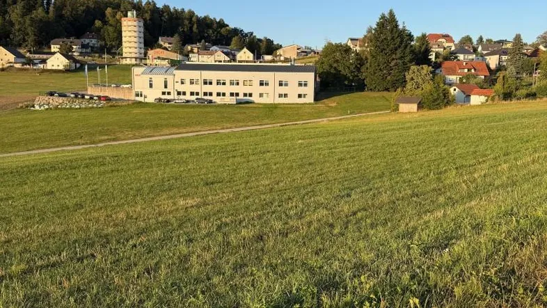 Weitläufige grüne Landschaft mit Blick auf ein Dorf und bewaldete Hügel unter klarem Himmel.