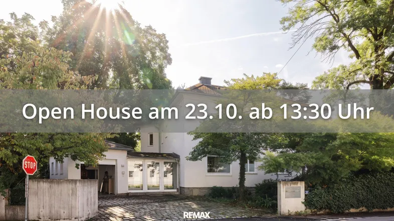 Helles Einfamilienhaus mit weißer Fassade, gepflasterter Einfahrt und umgebendem Grün.