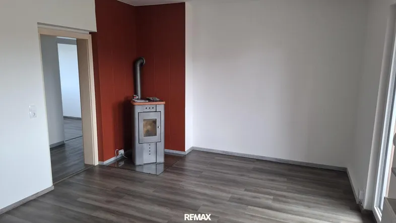 Heller Wohnraum mit modernem Holzofen, dunklem Laminatboden und roter Akzentwand.