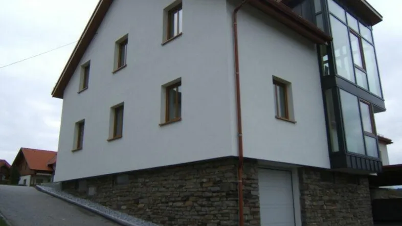 Ansicht des Hauses mit weißer Fassade, Steinsockel und modernem Glasanbau.