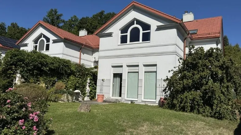 Weiße Reihenhäuser mit roten Ziegeldächern und gepflegtem Vorgarten unter blauem Himmel.