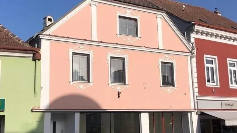 Historisches Gebäude mit rosa Fassade und traditionellen Stuckverzierungen, das eine charmante Straßenansicht bietet.