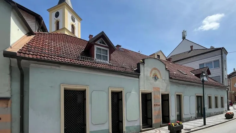 Altes Gebäude mit hellblauer Fassade, roten Ziegeldächern und einem Kirchturm im Hintergrund.