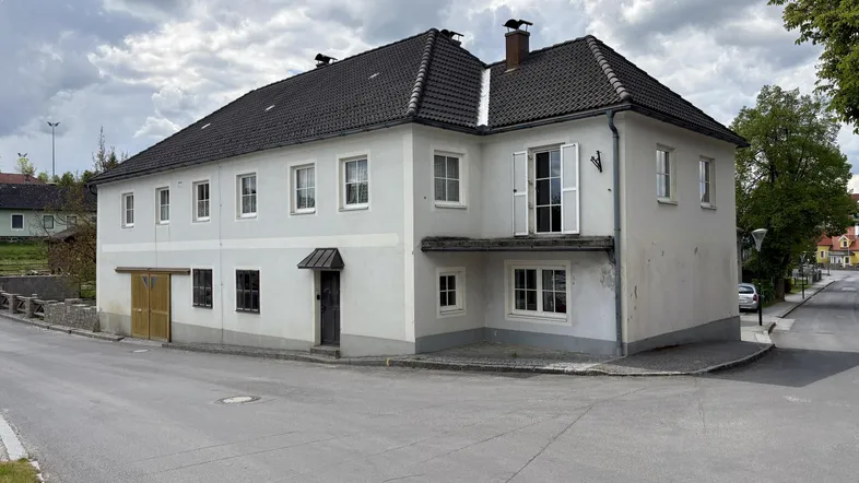 Historisches Gebäude mit weißer Fassade, dunklem Ziegeldach und einem französischen Balkon an der Straßenecke.