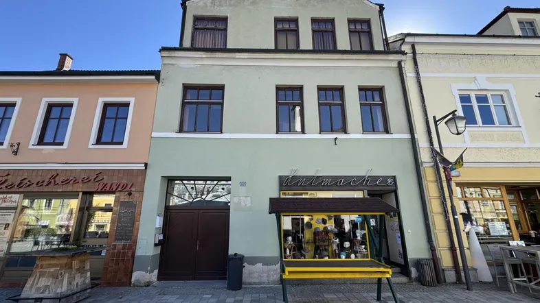 Historisches Gebäude mit hellgrüner Fassade und braunen Fenstern an einer belebten Straße.
