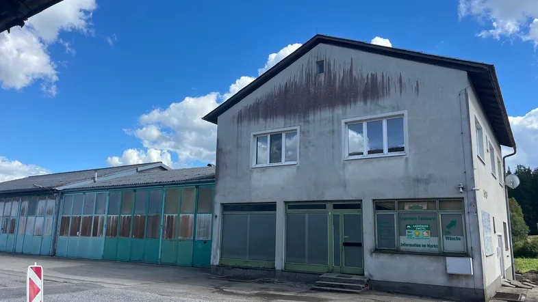 Ansicht eines älteren Geschäftsgebäudes mit angrenzender Industriehalle unter blauem Himmel.
