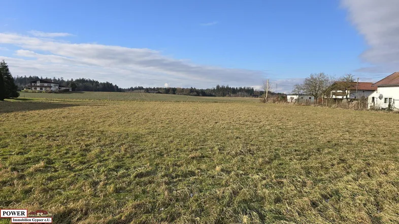Weitläufiges Feld mit Blick auf die umliegende Landschaft und vereinzelte Häuser unter blauem Himmel.