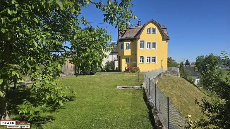 Gelbes Haus mit Mansarddach und großem Garten auf einem sonnigen Grundstück mit Weitblick.