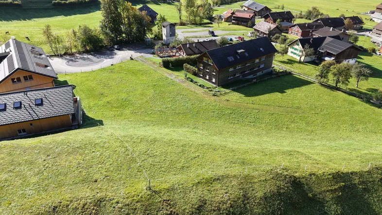 Luftaufnahme eines ländlichen Anwesens mit grünen Wiesen und umliegenden Häusern in einer Berglandschaft.