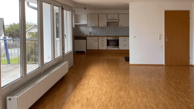 Heller offener Wohn-Essbereich mit Parkettboden und Zugang zum Balkon, inklusive integrierter Küche.